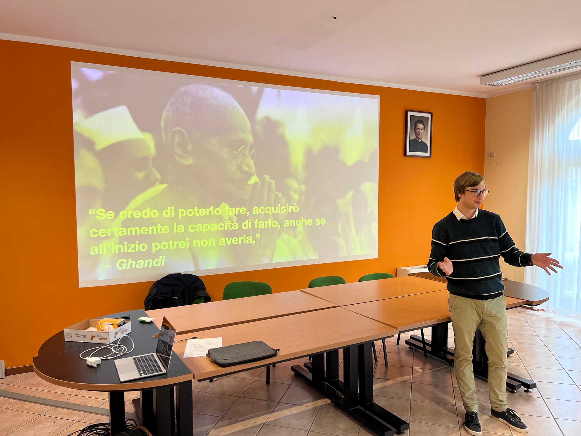 Stefano che spiega ad una classe di studenti. La slide mostra una citazione di Ghandi a scopo goliardico.